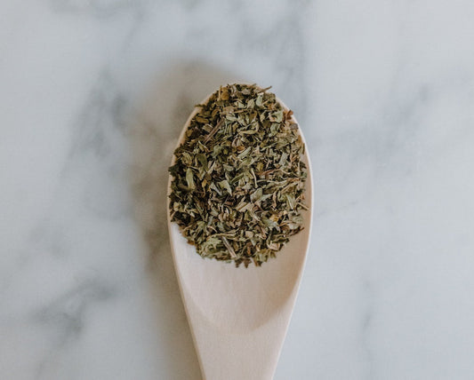 wooden spoon filled with dried herb, set ontop of a white marble countertop